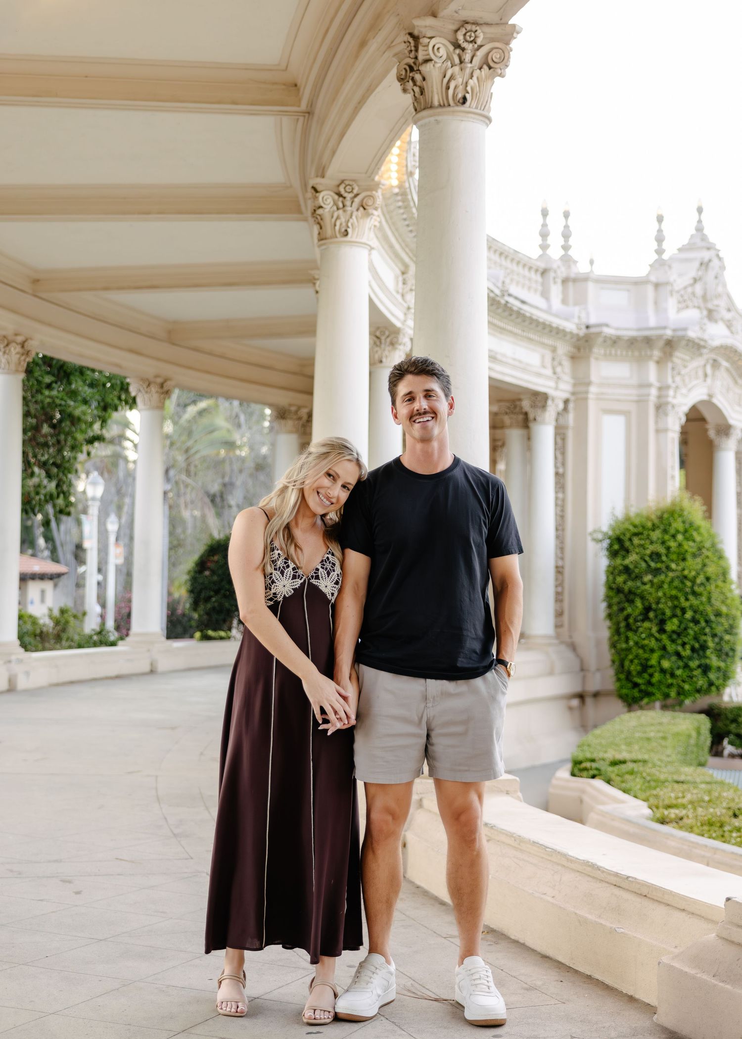 A couple posing together in front of elegant white columns and archways.