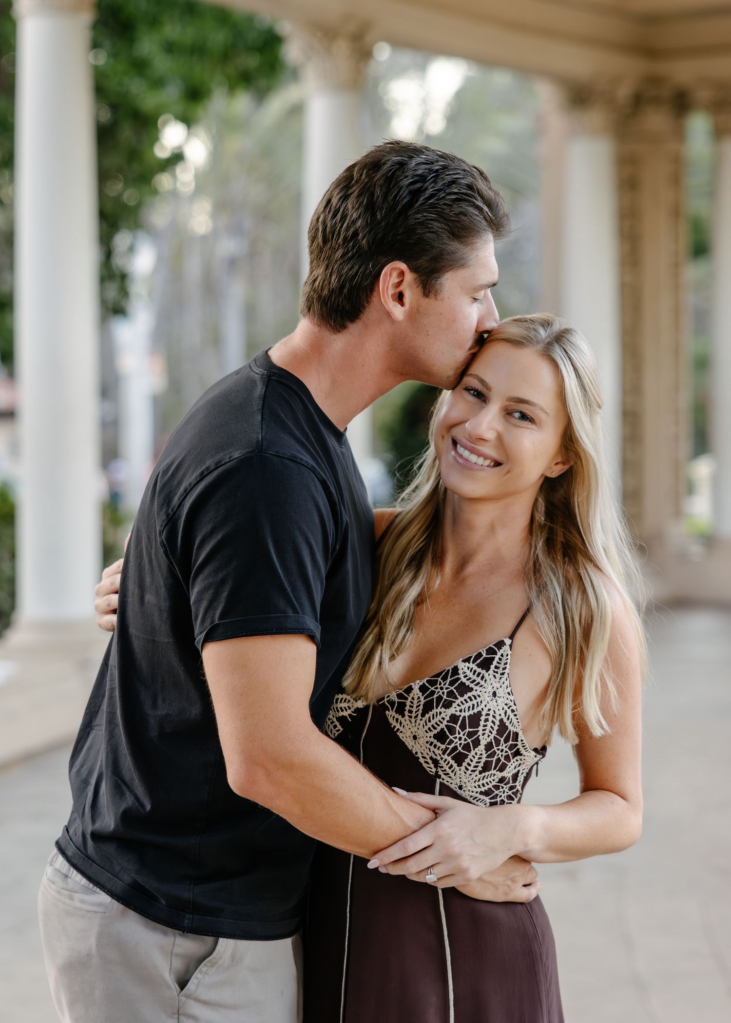 A couple sharing playful moments beneath ornate white columns and architecture.