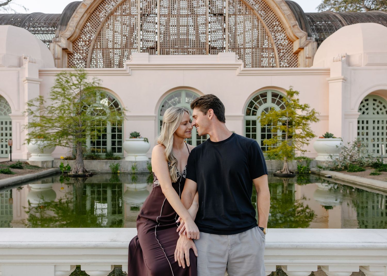 A couple shares a romantic moment near an elegant granite balustrade in a garden setting.