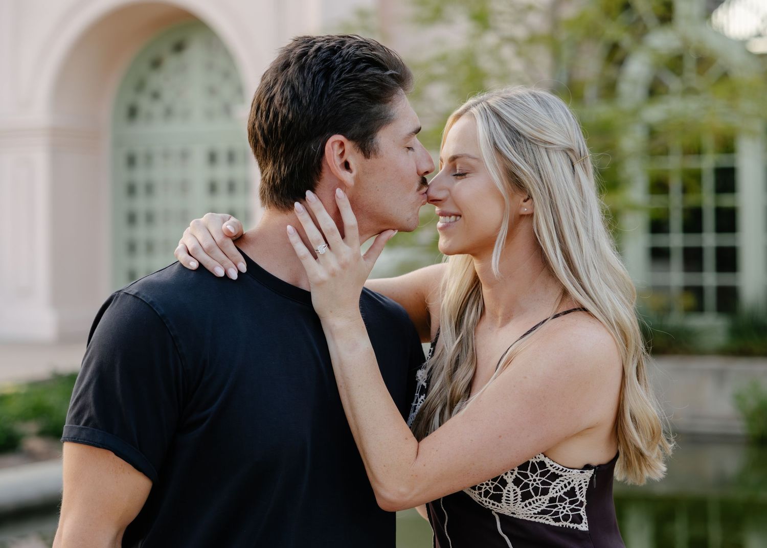 A couple shares an intimate kiss against an elegant architectural backdrop with columns.