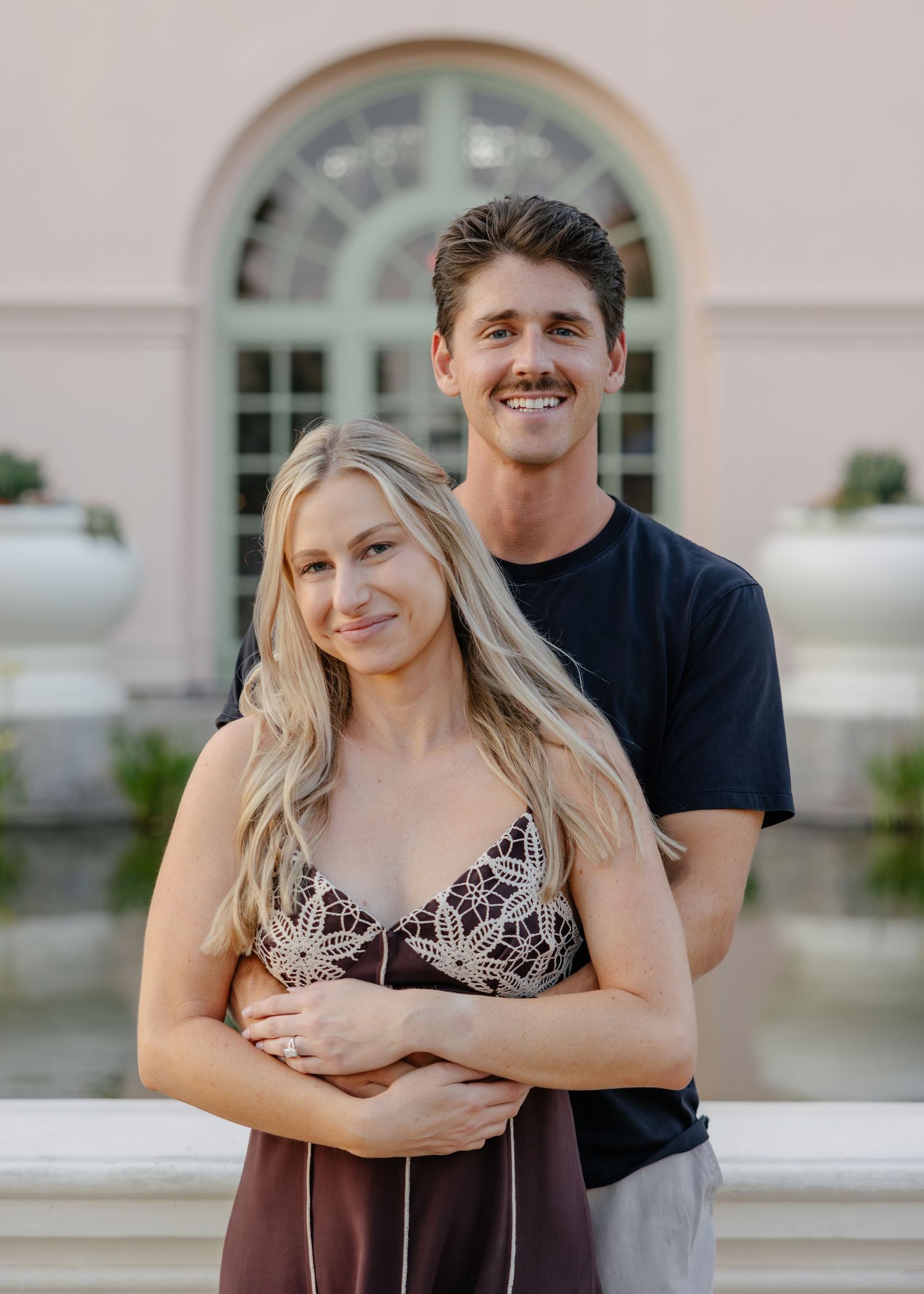 A couple embracing and smiling in front of a classical white building facade.