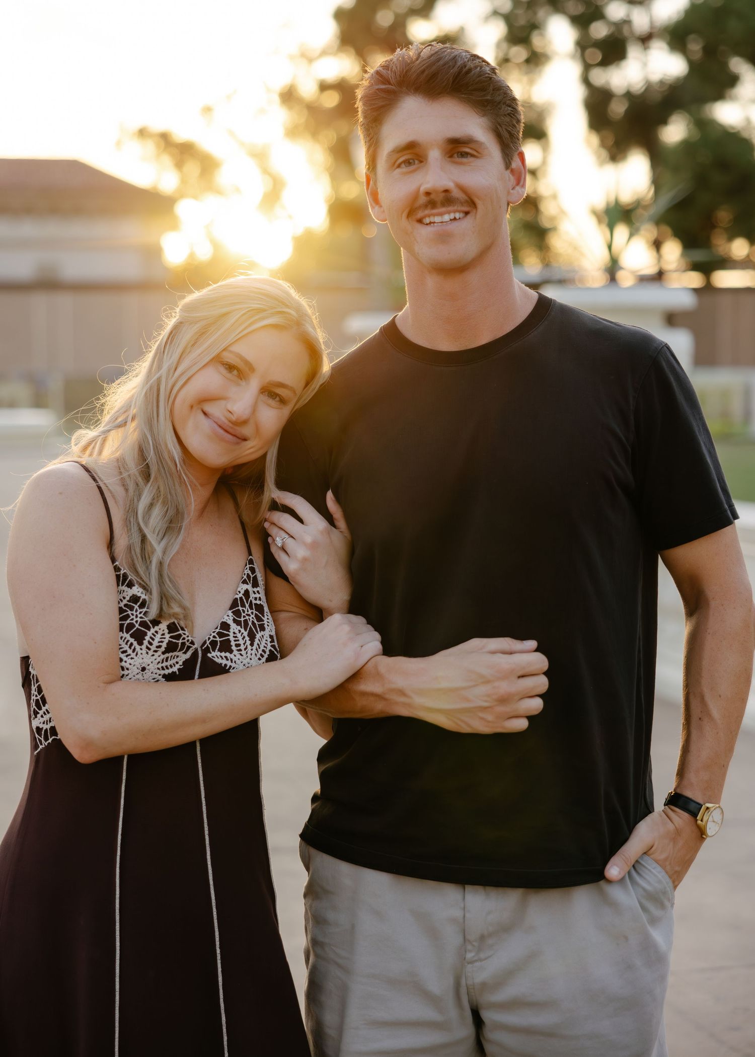 Couple laughing and embracing outdoors during golden hour sunset while wearing casual attire.