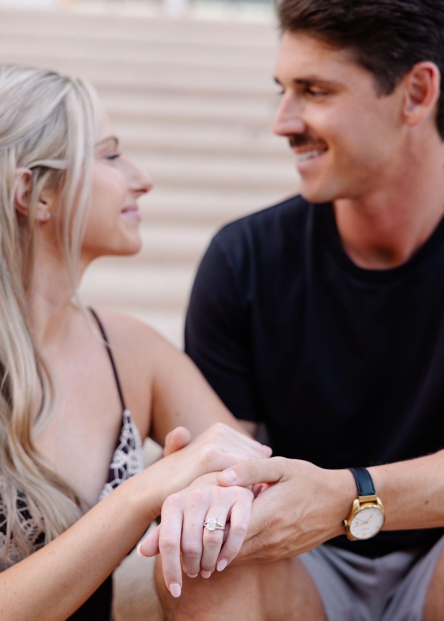 Closeup shot of hands coming together with engagement ring visible against a neutral background.