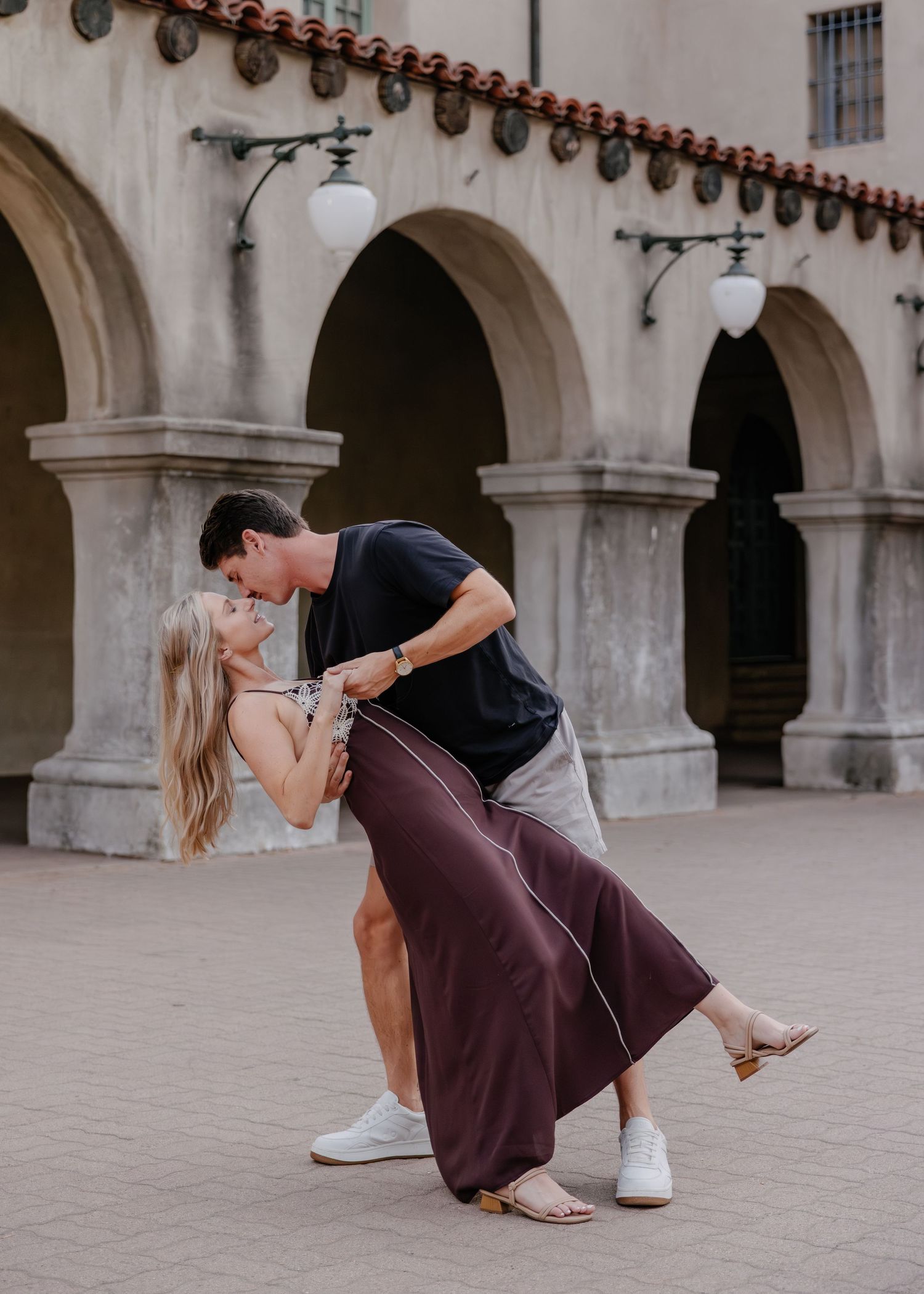 Couple playfully interacting on steps in front of an arched colonial style building.
