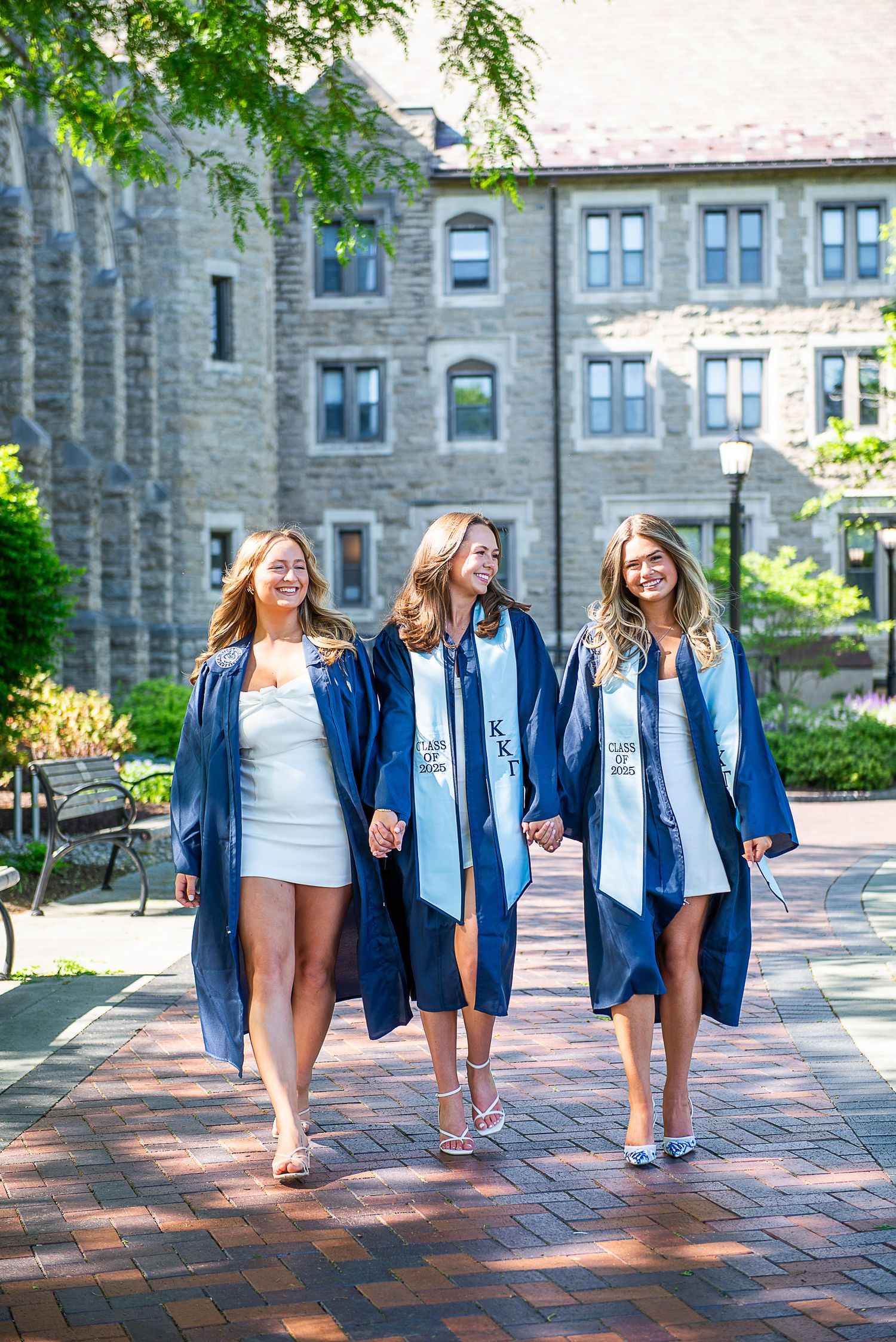 People in matching denim jackets walk together on a brick path outside a stone university building.