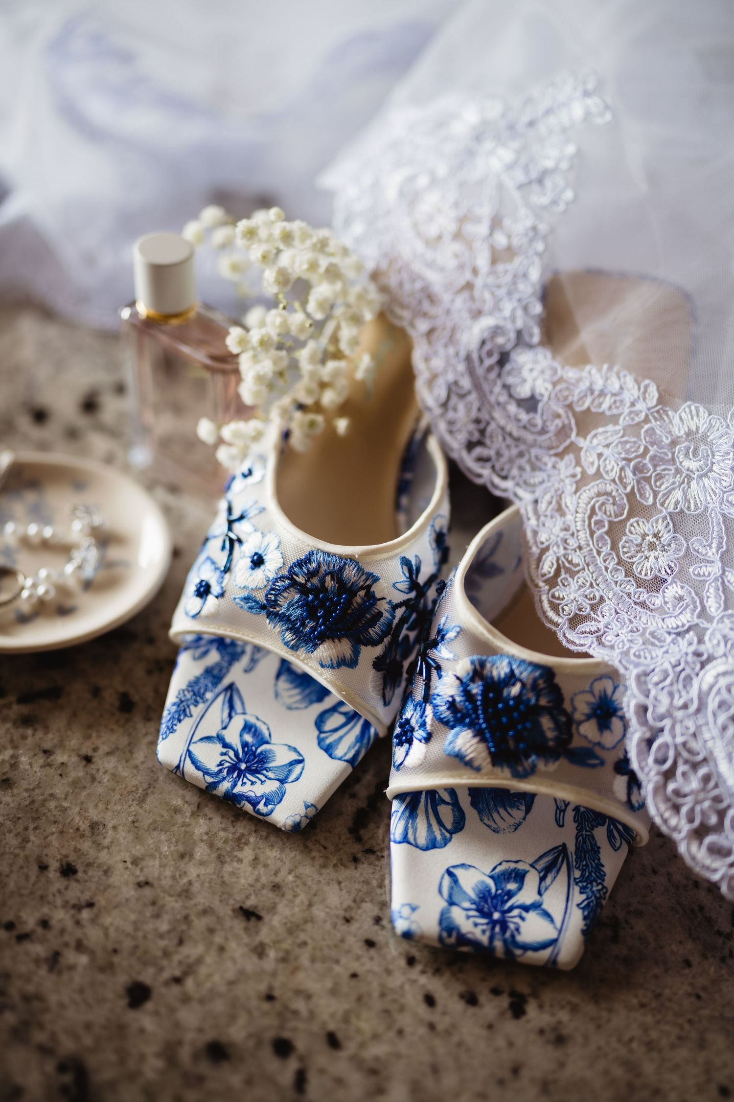 Delicate white baby booties with blue floral pattern and lace trim arranged on textured surface in various angles.