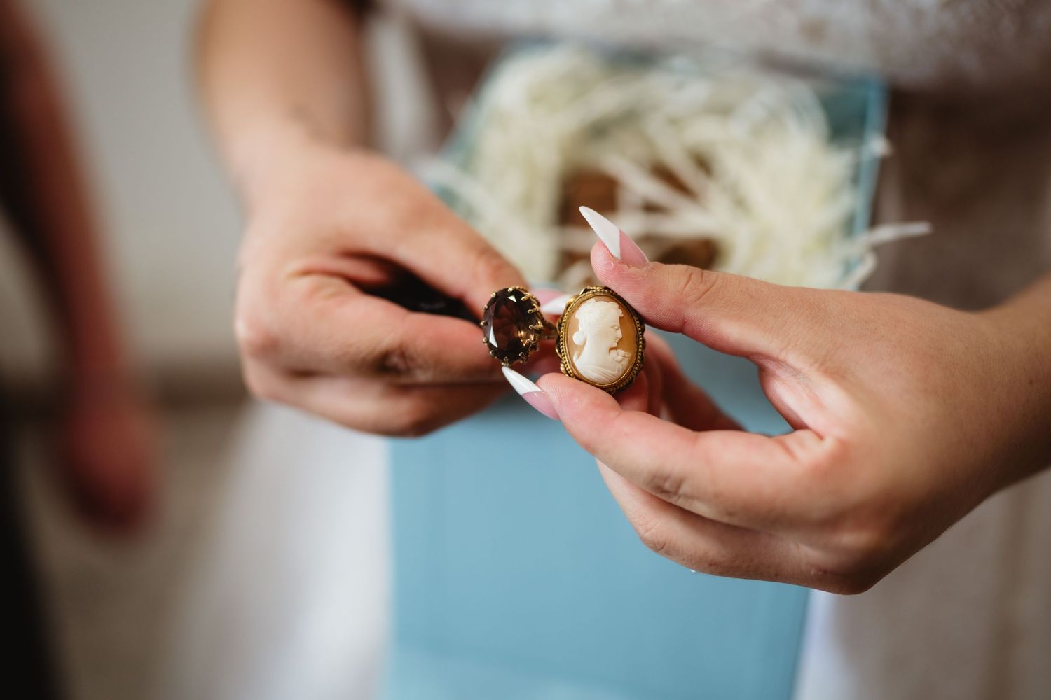 Close-up shot of hands holding and examining a small delicate object against a soft blue background.