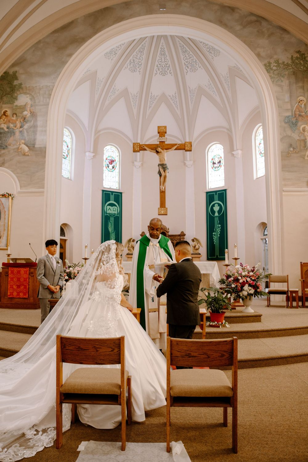 A Catholic church interior with white walls, vaulted ceilings, wooden pews and green banners during a wedding ceremony.