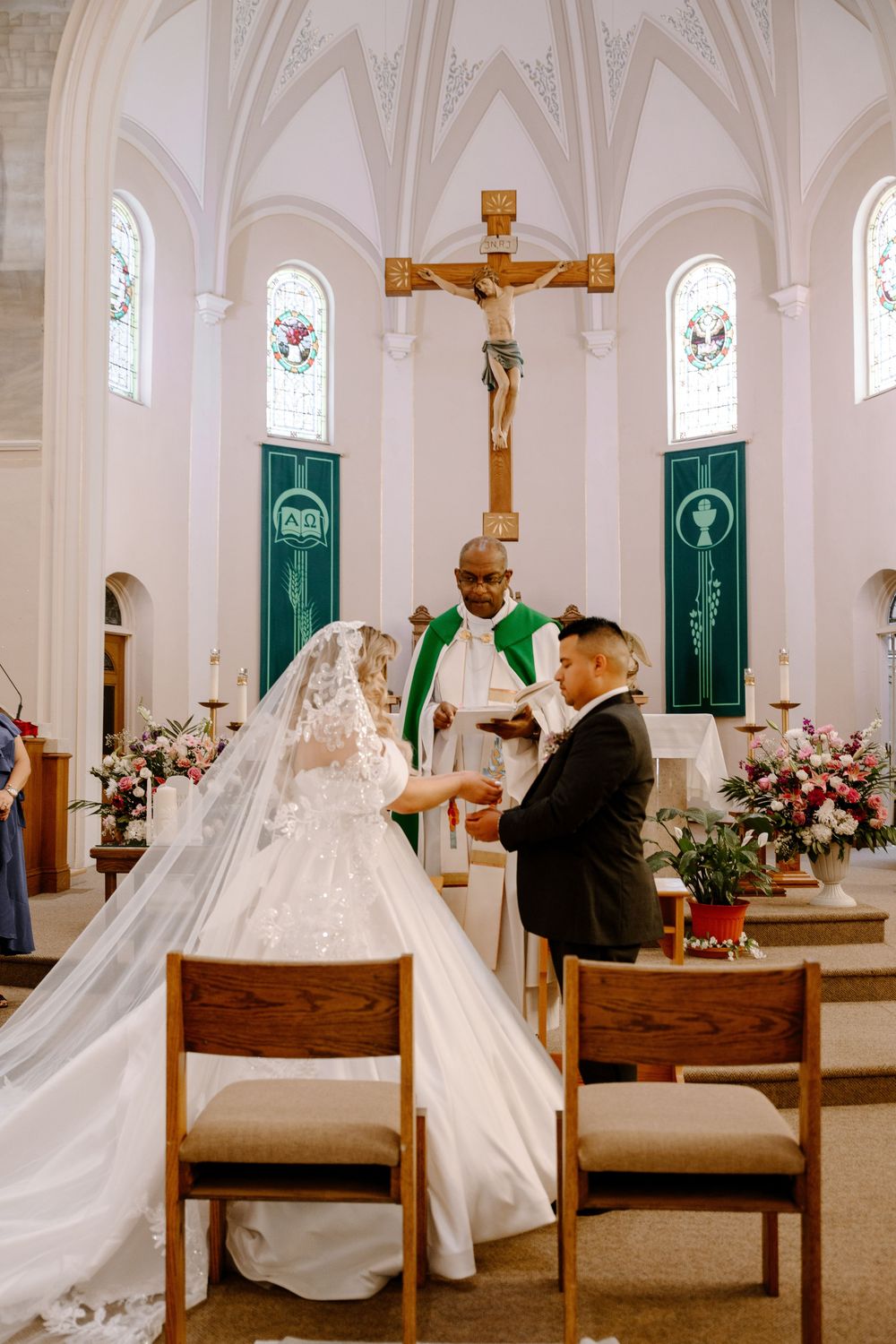 A wedding ceremony scene in a white church interior with ornate vaulted ceilings, wooden pews, and green door accents.