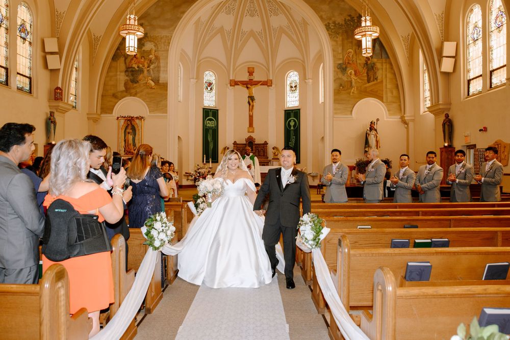 A catholic wedding ceremony inside an ornate church with white pillars and traditional religious decor.