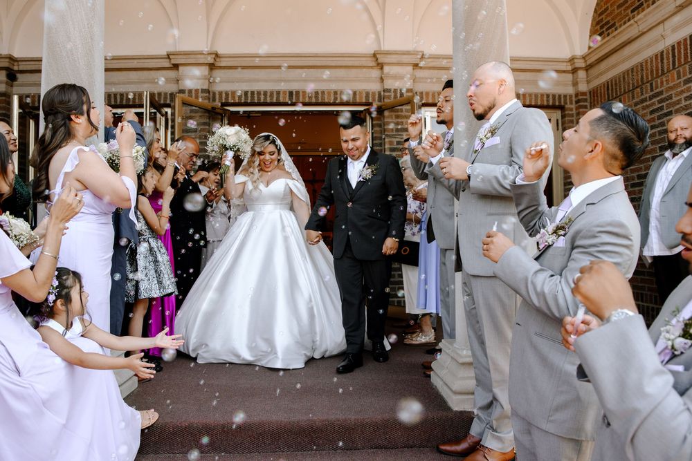 Wedding guests dance and celebrate at an elegant indoor reception venue with ornate architecture.