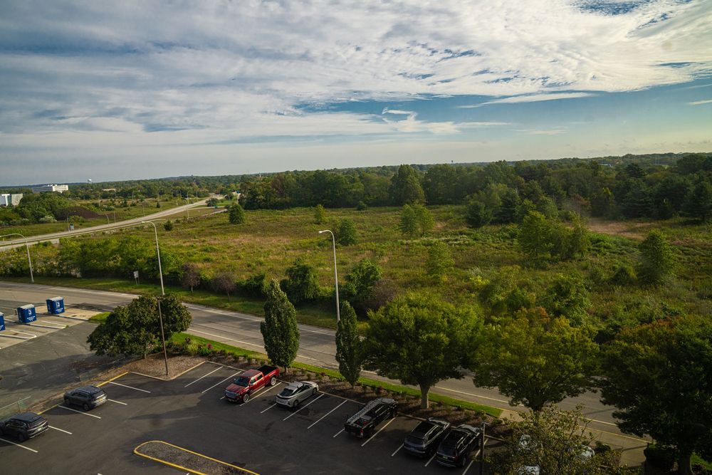 Aerial view of a parking lot surrounded by green landscape and roads under a cloudy sky.