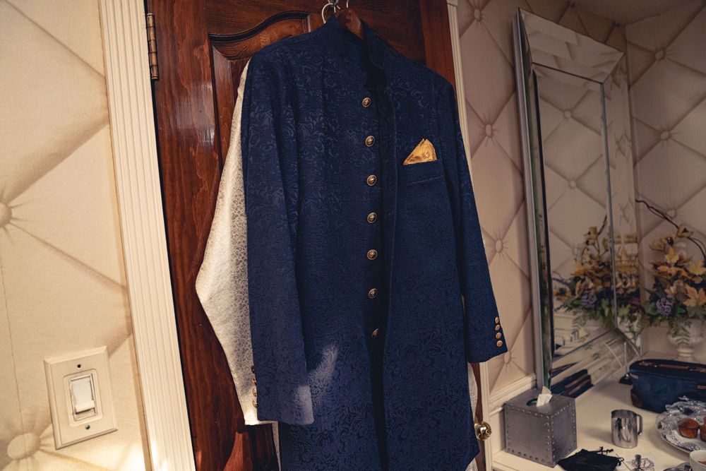 Navy blue formal dress coat hanging on wooden door with orange pocket square accent. Wedding at Westbury Manor