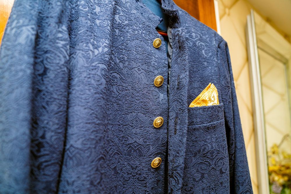 Close up detail of a navy blue textured jacket with brass buttons and yellow pocket square. Wedding at Westbury Manor