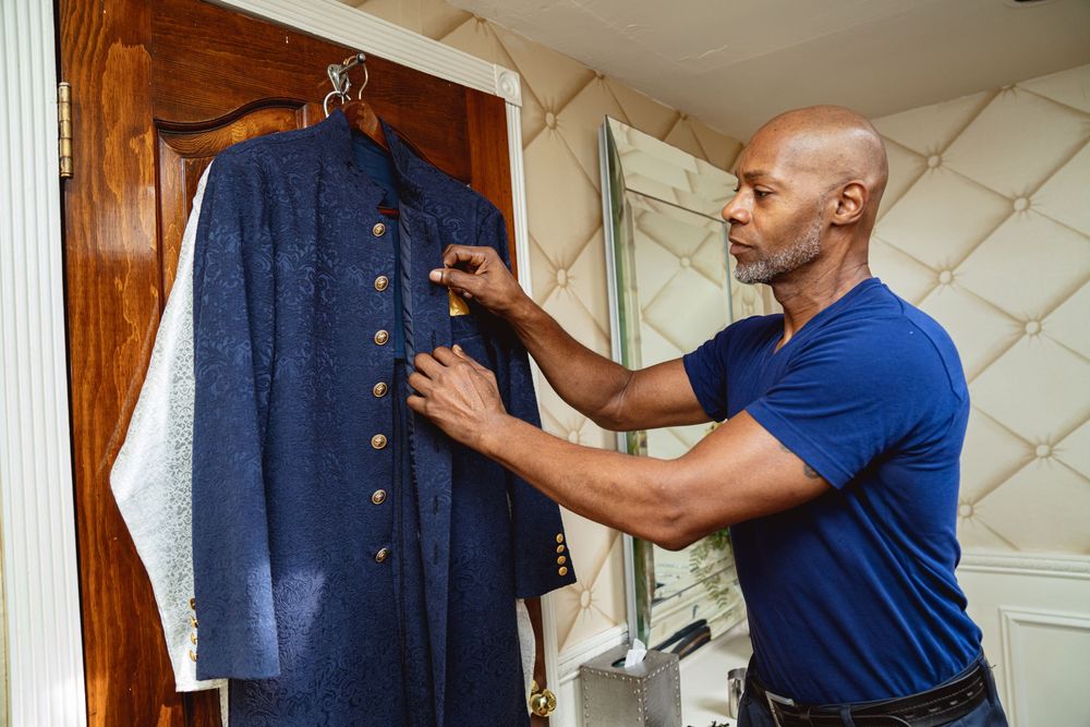 Person wearing blue shirt inspects and adjusts buttons on a navy blue jacket hanging on wooden cabinet. Wedding at Westbury Manor