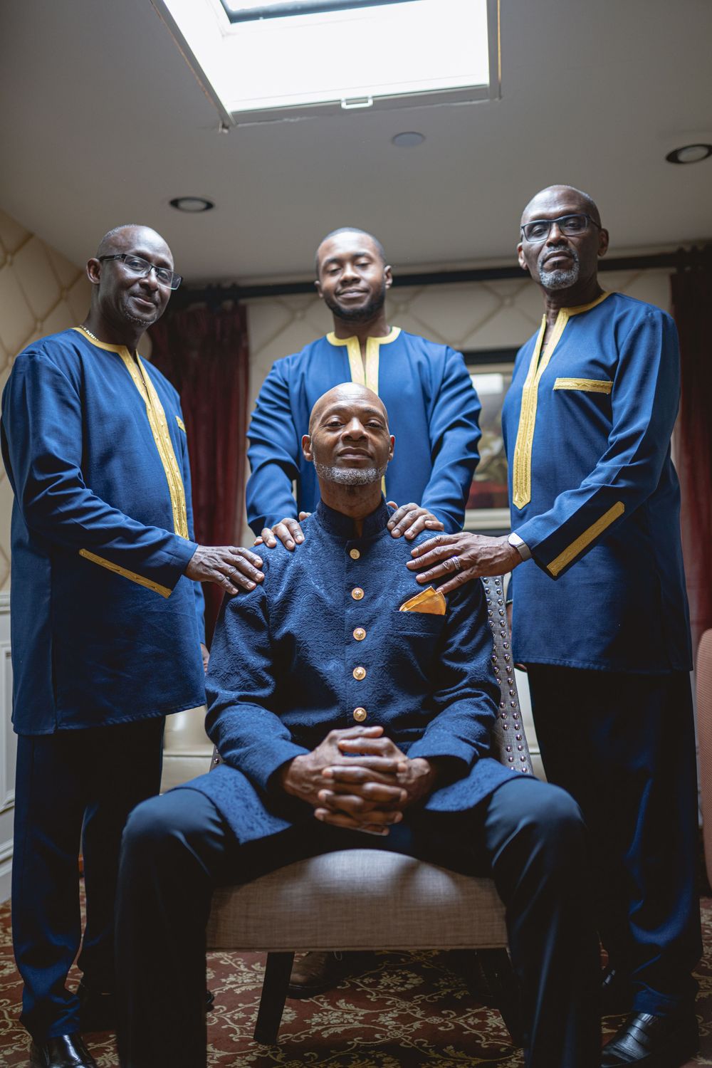 Four men pose together wearing matching navy blue and yellow formal suits against an indoor backdrop. Wedding at Westbury Manor