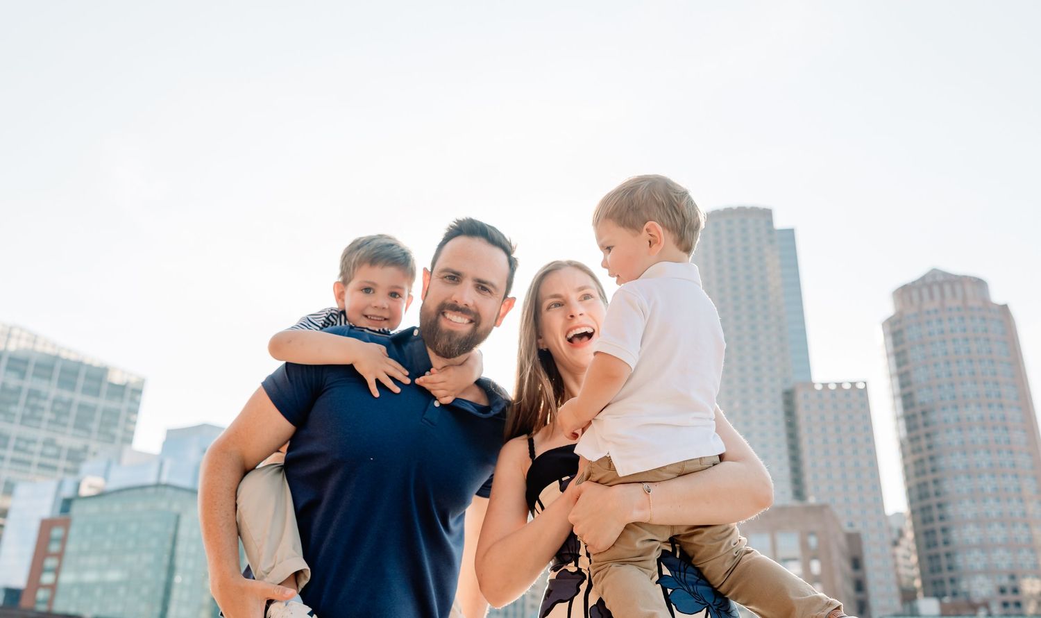 A family with their child shares joyful moments together against a backdrop of tall urban buildings.