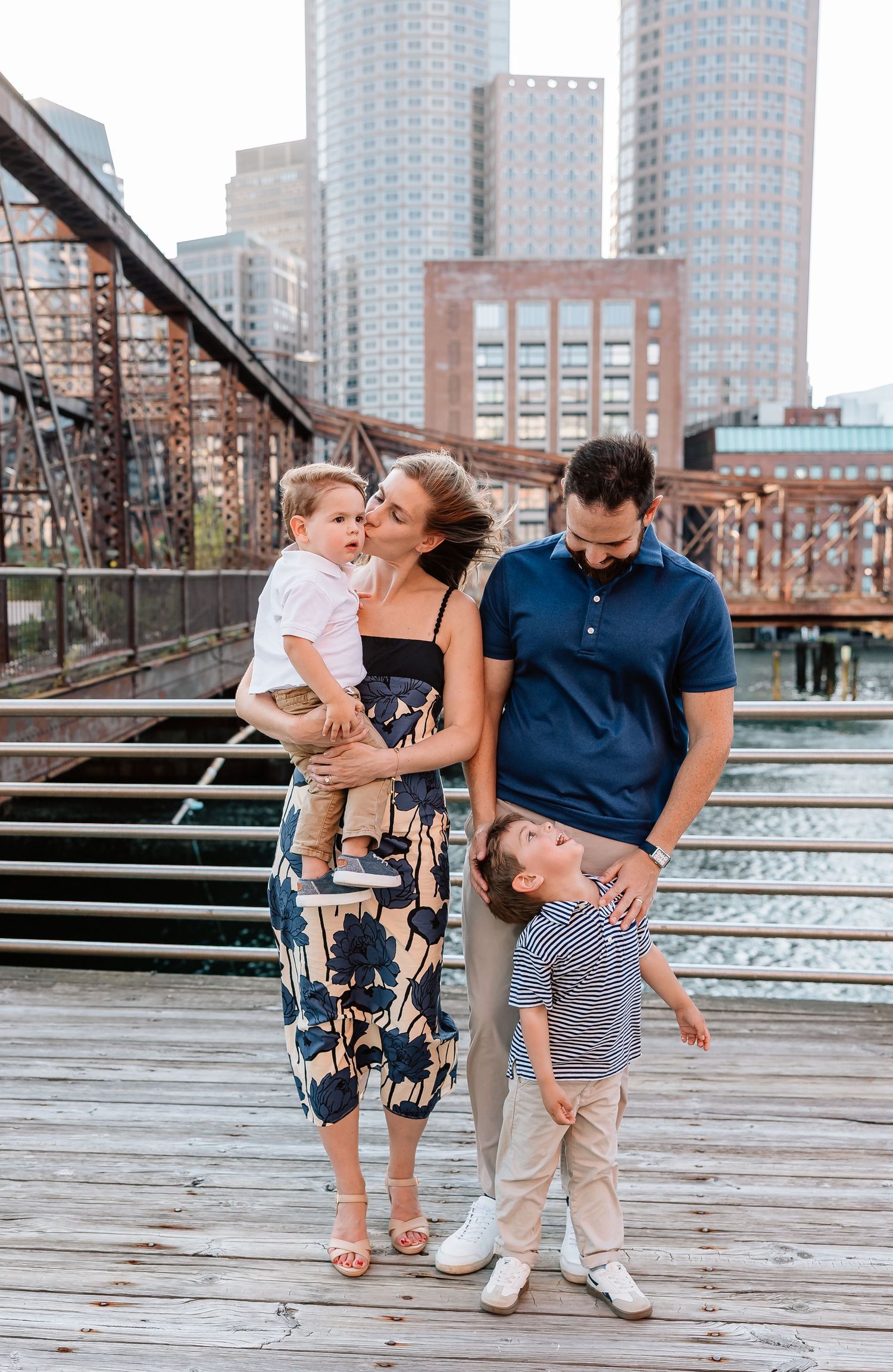 Family spending time together while posing at Long Island City waterfront with urban skyline in background.