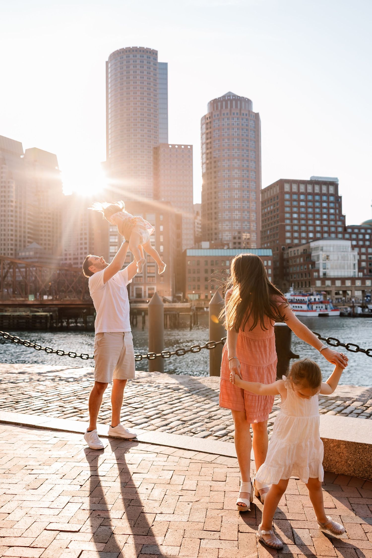 Dancing silhouettes enjoying sunset on brick waterfront with Boston skyline in the background.