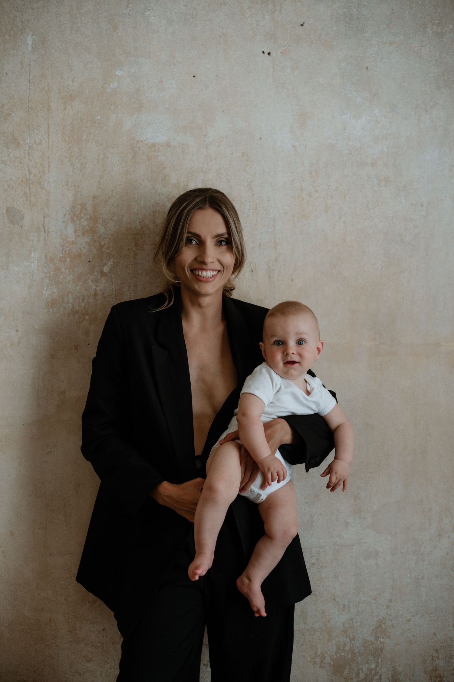 Artistic black and white portraits showing a woman in business attire holding an infant against a textured wall.