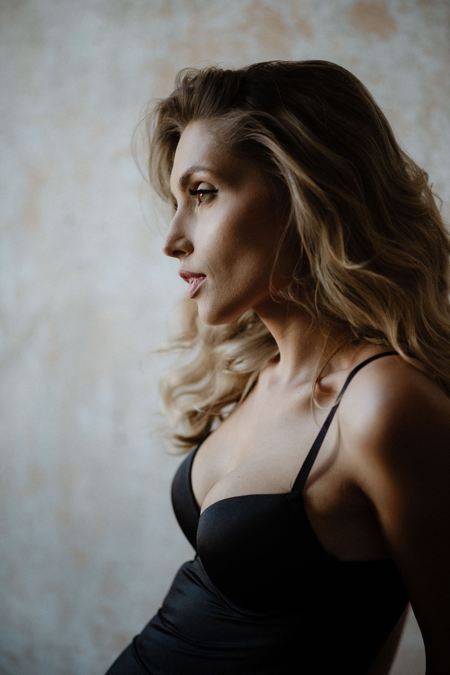 Artistic boudoir photo series showing moody profile poses against textured wall in black lingerie.