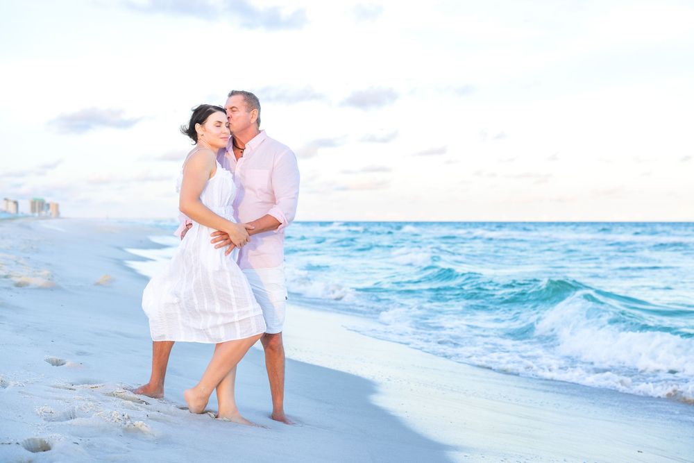 A couple in white clothing shares romantic moments along a beautiful tropical beach with turquoise waters.