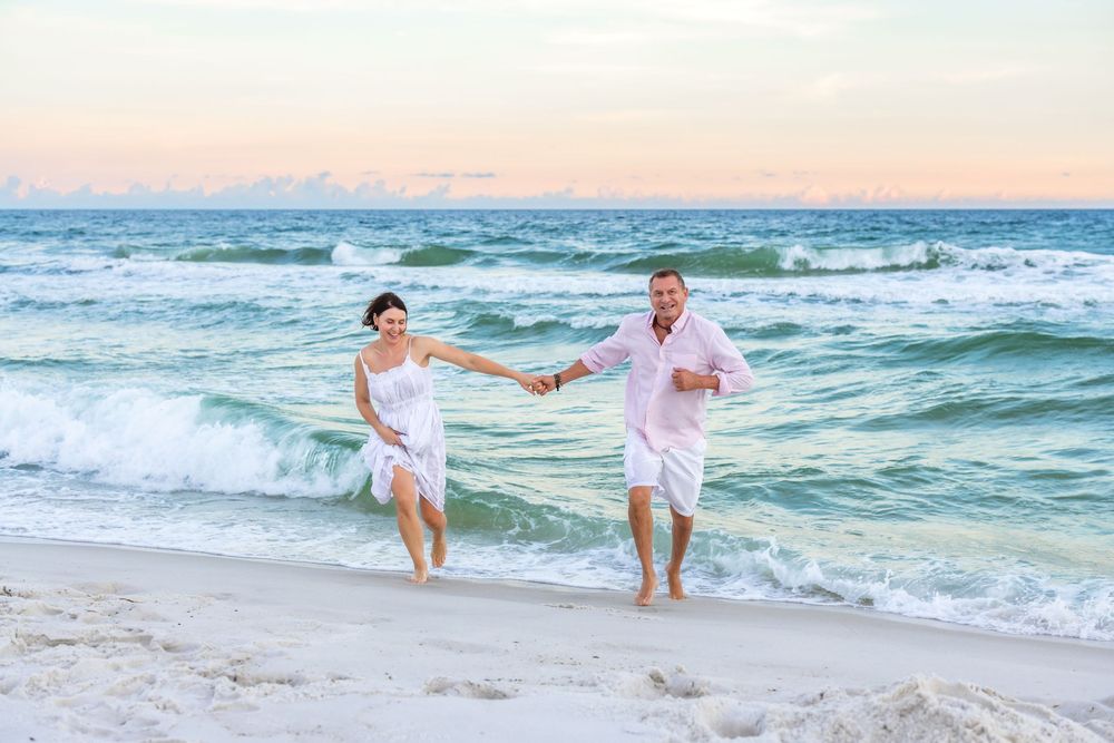 Beachgoers splashing and playing together in the blue ocean waves during a pink sunset on a sandy beach.