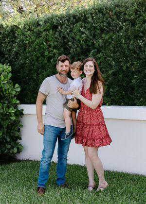 Family enjoying time together against white wall and green landscaping.