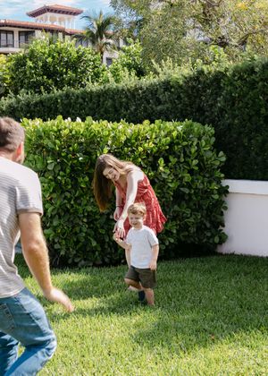 Active family playing and running on green lawn near manicured hedges.