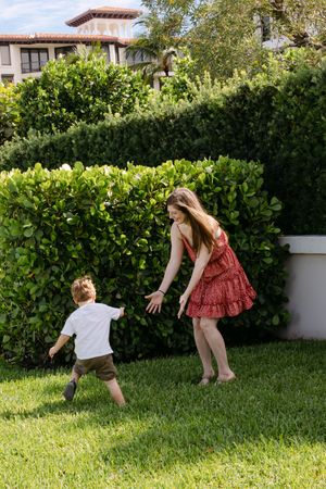Playful family moment captured in sunny backyard with hedge backdrop.