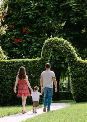 A family walks together on a garden path surrounded by lush greenery and hedges.
