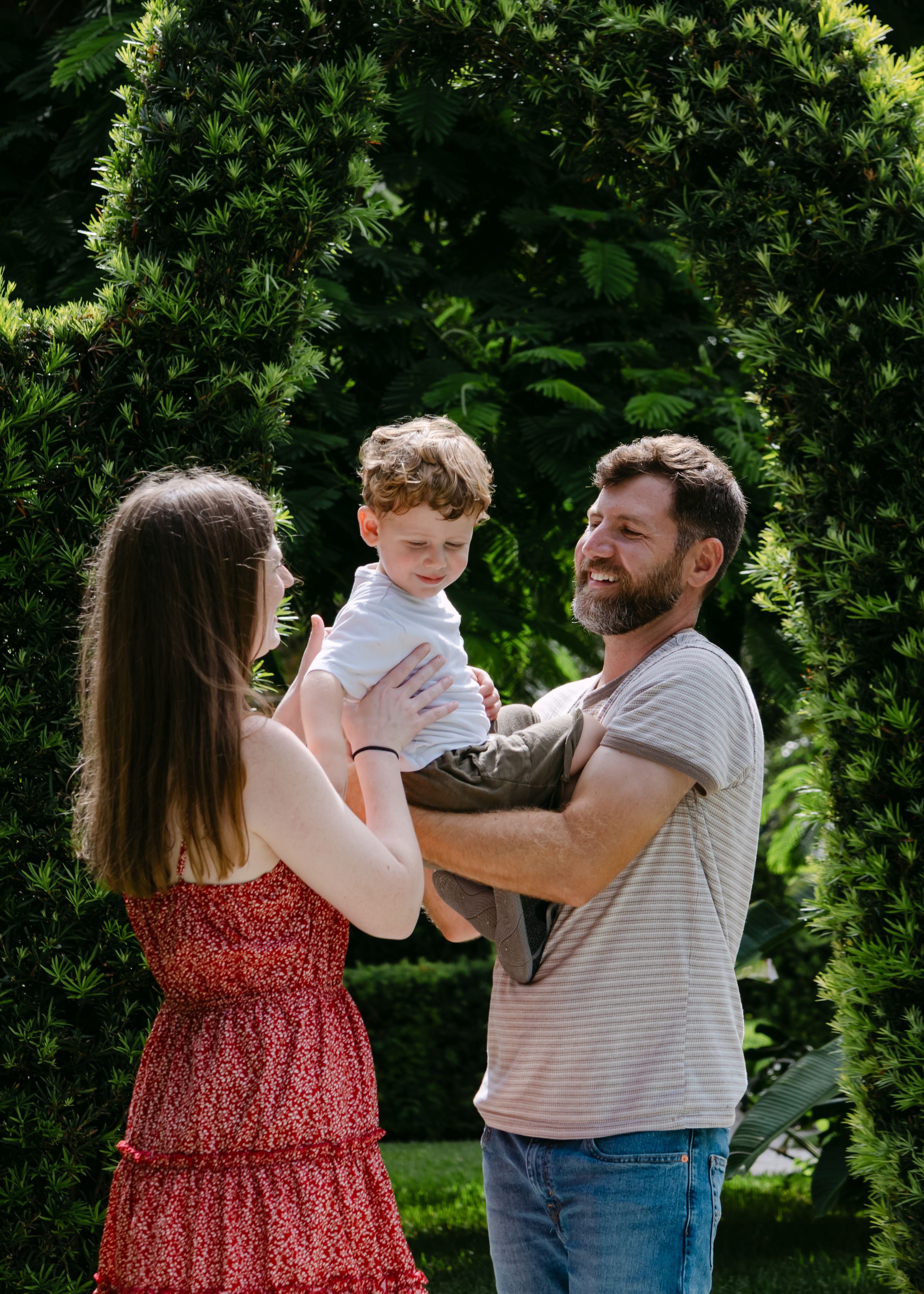 A group shares playful moments together on a grassy lawn with hedges in the background.