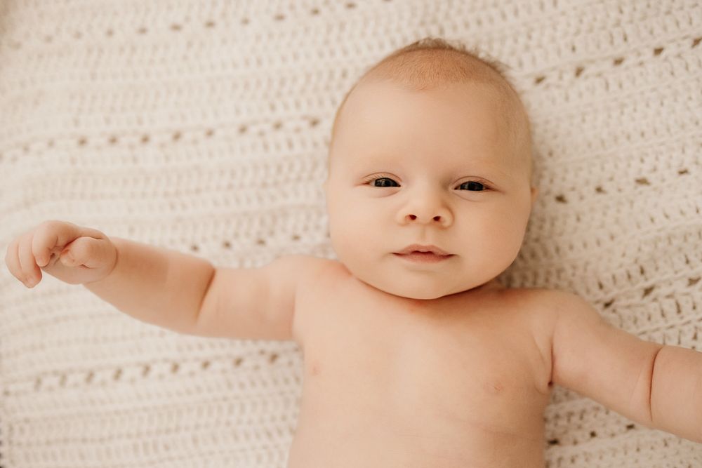 Newborn baby boy lays on a knitted blanket while looking into the camera during his lifestyle newborn photos in Los Altos Hills