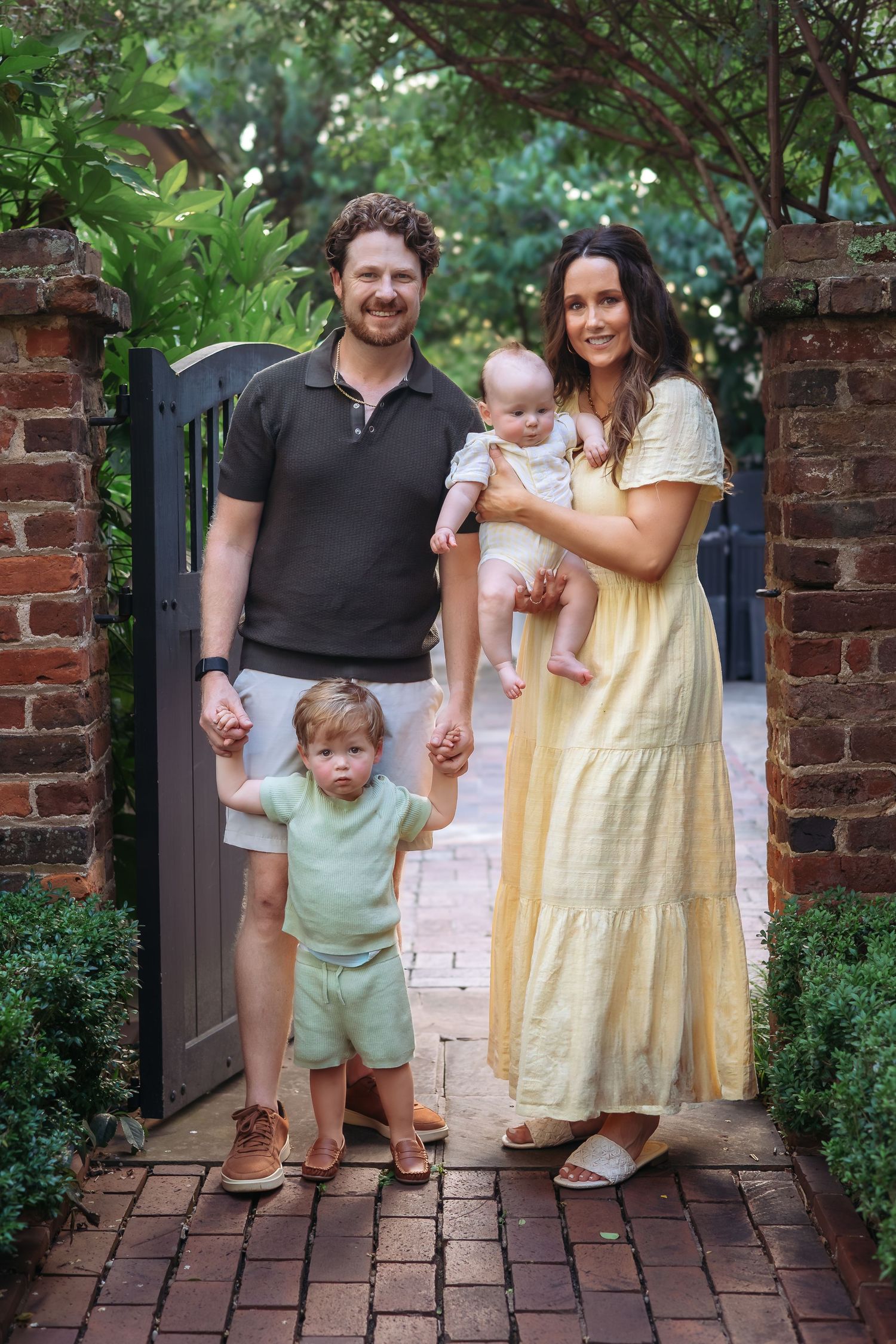 Family of 4 smiling at camera by brick wall during family photography session in Athens GA