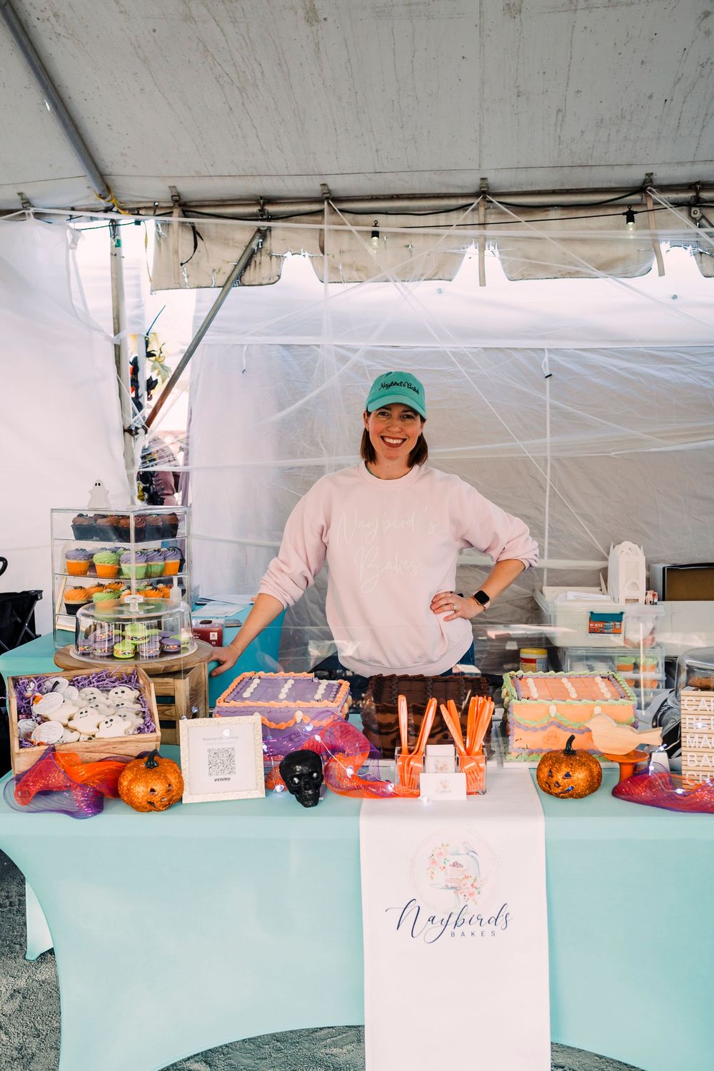 A vendor stands behind a booth at a seasonal market with pumpkins, candy and other Halloween-themed merchandise on display.