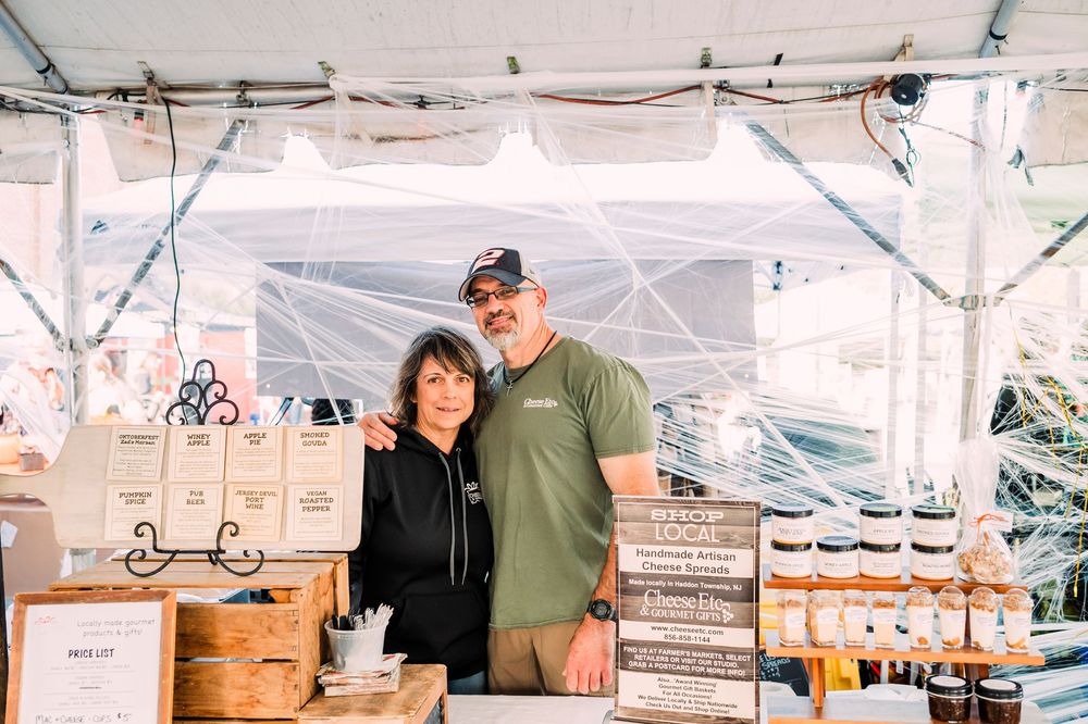 Customers shopping at a large farmers market booth displaying local food products and produce.