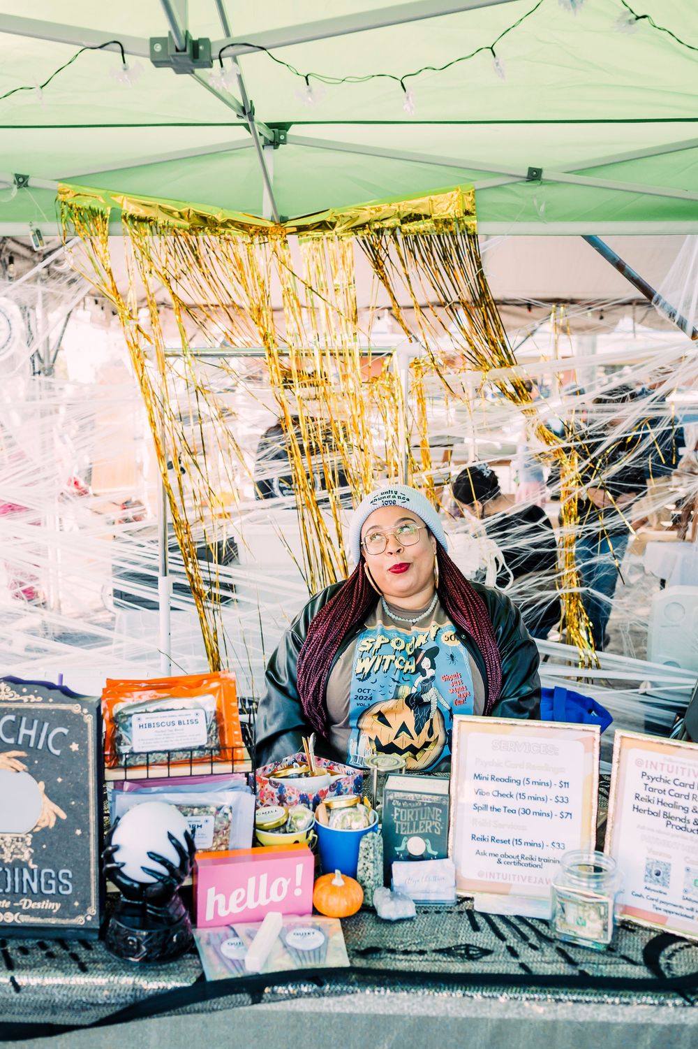 A festive Halloween-themed vendor booth with gold tinsel decorations and spooky merchandise on display.