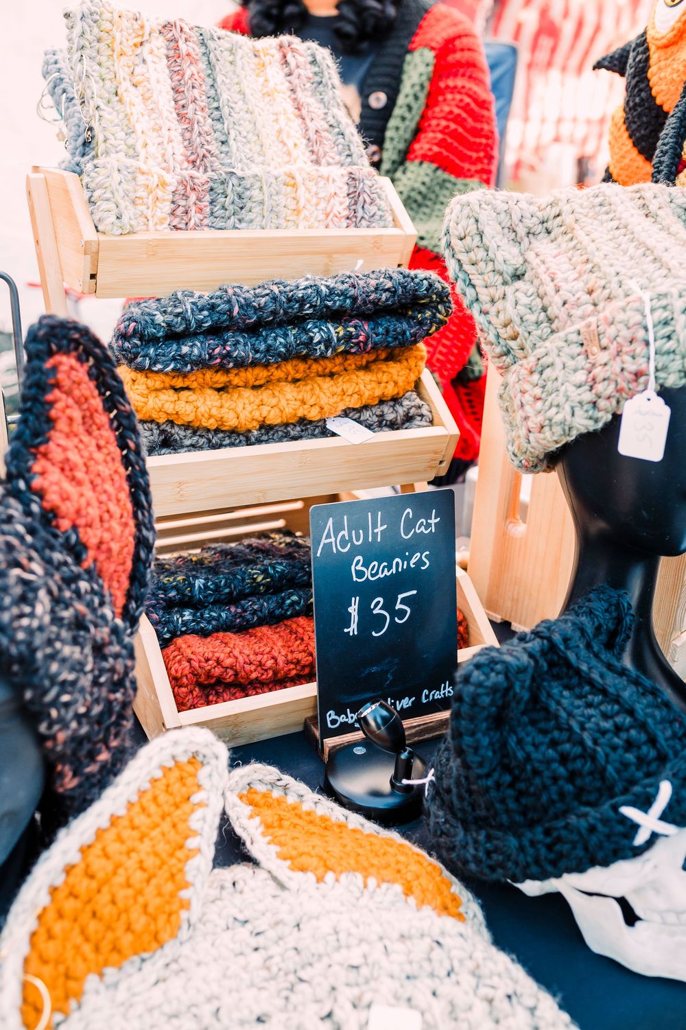 Close-up view of chunky knit blankets and crochet accessories displayed at a market stall with price tags.