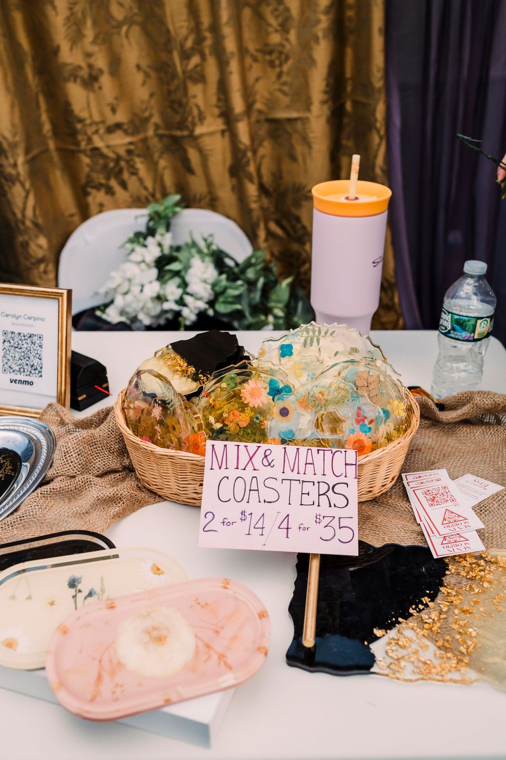 Wedding merchandise display featuring coasters, drinks and decorations on a table with a gold curtain backdrop.