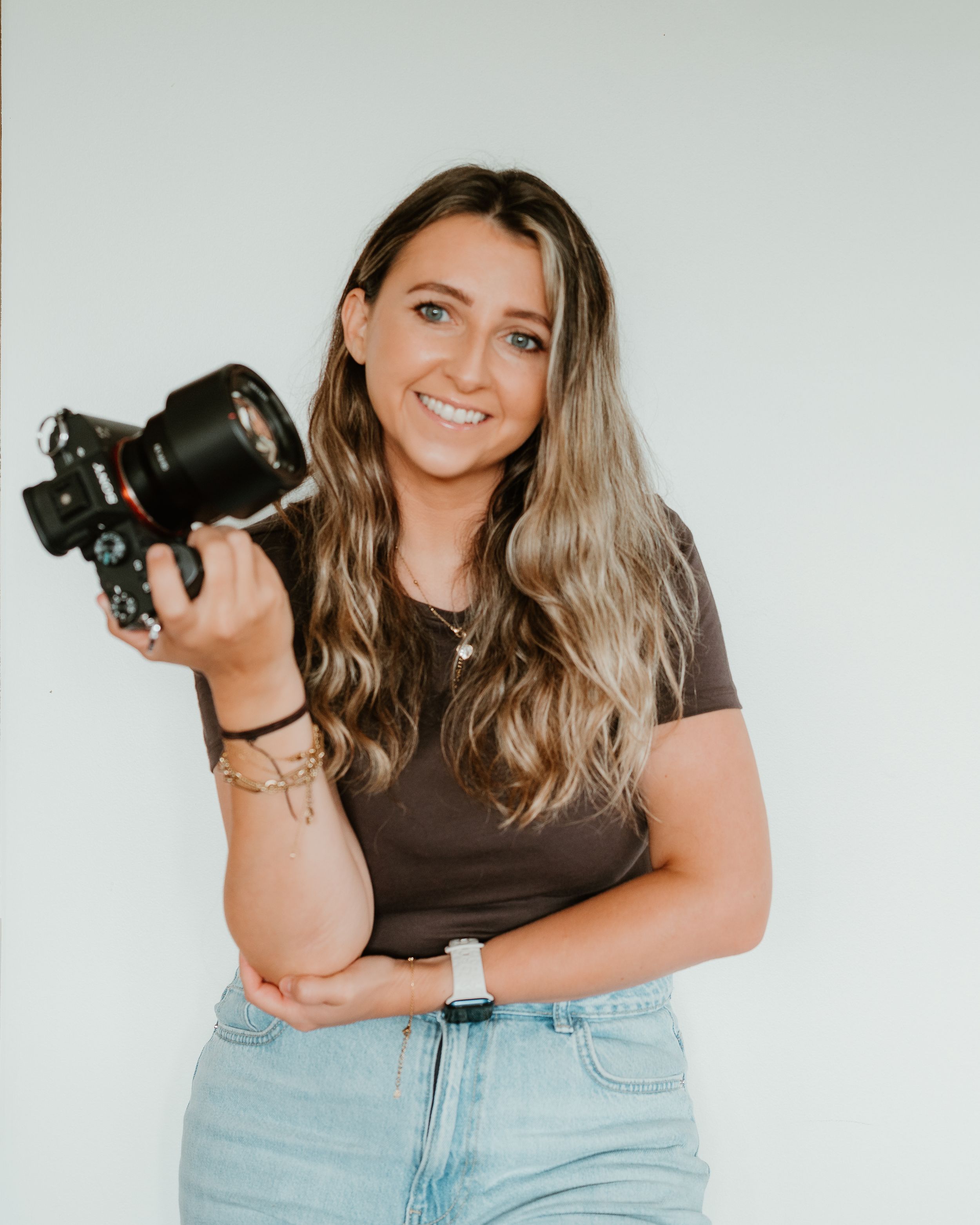 Lifestyle photographer holding professional camera equipment against white studio background.