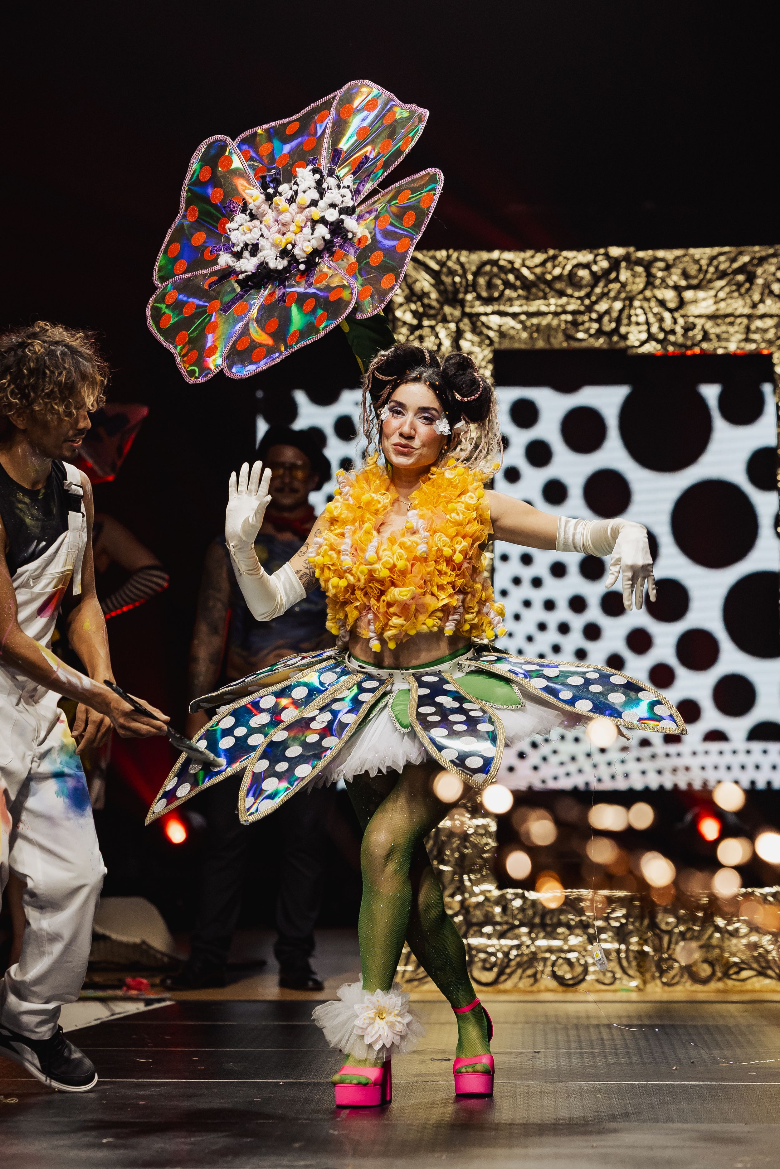 Colorful polka dot backdrop frames performer in bright costume during dynamic stage show.