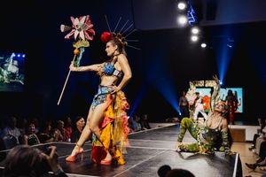 Performers dance energetically in colorful costumes on a dark stage with dramatic blue lighting effects.