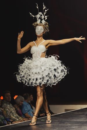 Fashion model walks runway in fluffy white tulle tutu dress and headpiece during avant-garde fashion show performance.