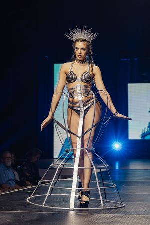Fashion model walks runway in avant-garde geometric cage dress design at futuristic fashion show with blue lighting.