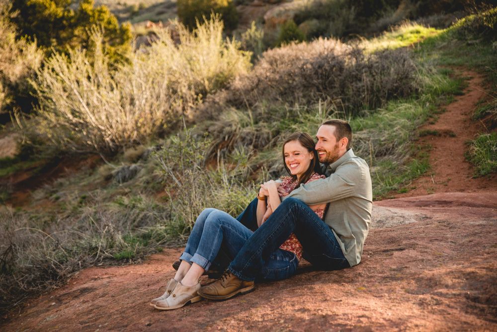 Couple sitting on dusty red rock formations during golden hour in a scenic outdoor desert setting with hiking trails.