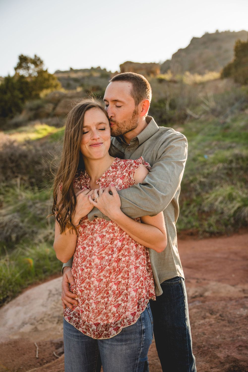 A couple embraces on a rustic dirt trail during a romantic outdoor photoshoot at sunset.