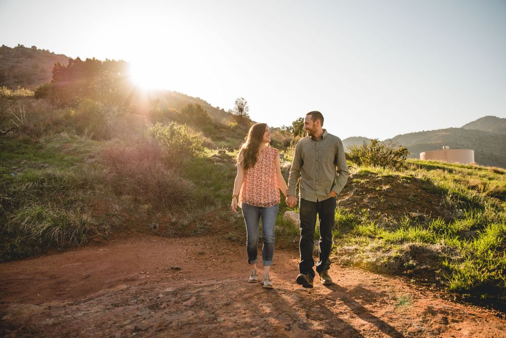 Couple walking hand in hand on a sunlit hiking trail through rolling hills during golden hour.