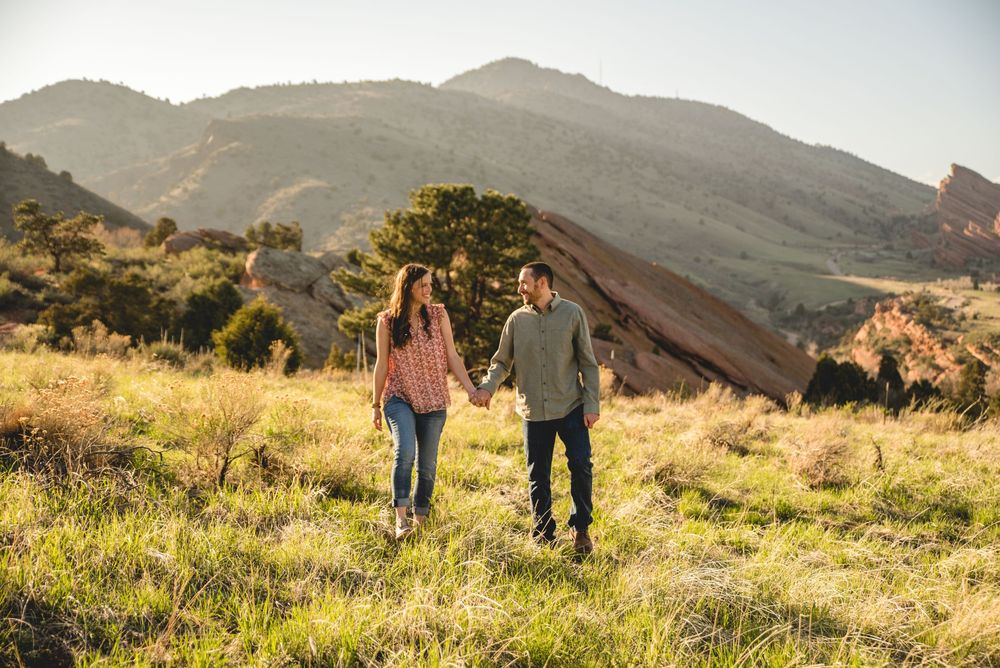 Panoramic view of people walking along a scenic hillside trail during golden hour with mountains in the background.