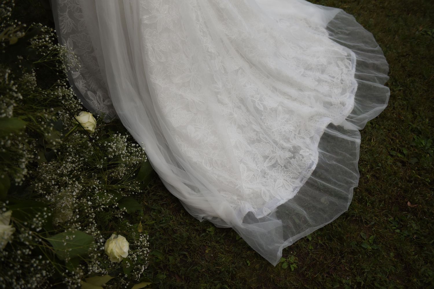 Flowing white wedding dress details with tulle and lace on grass.