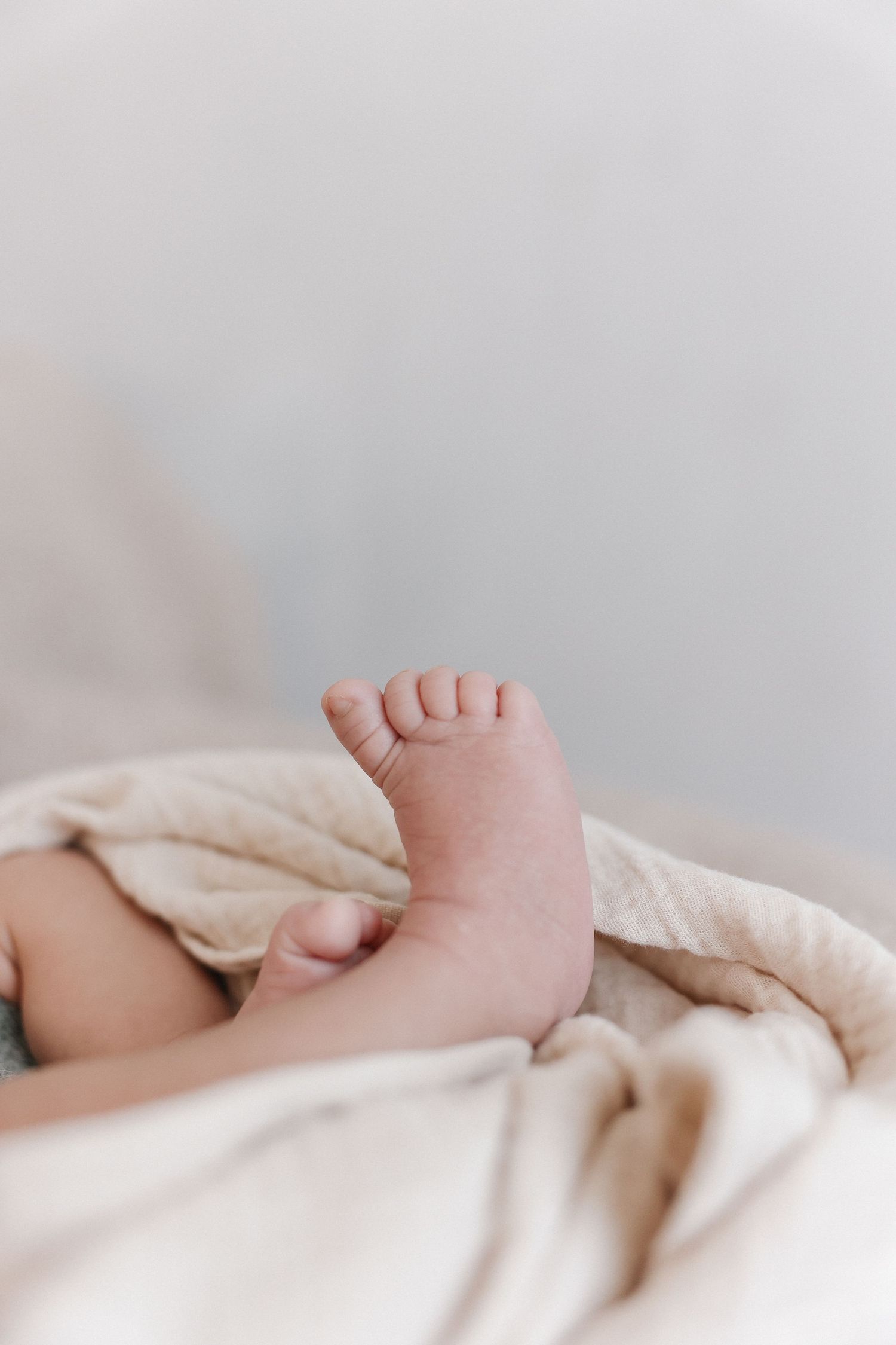 Close-up of soft baby toes and foot peeking out from white cotton bedding for Lifestyle newborn session at Spark Studios, OC